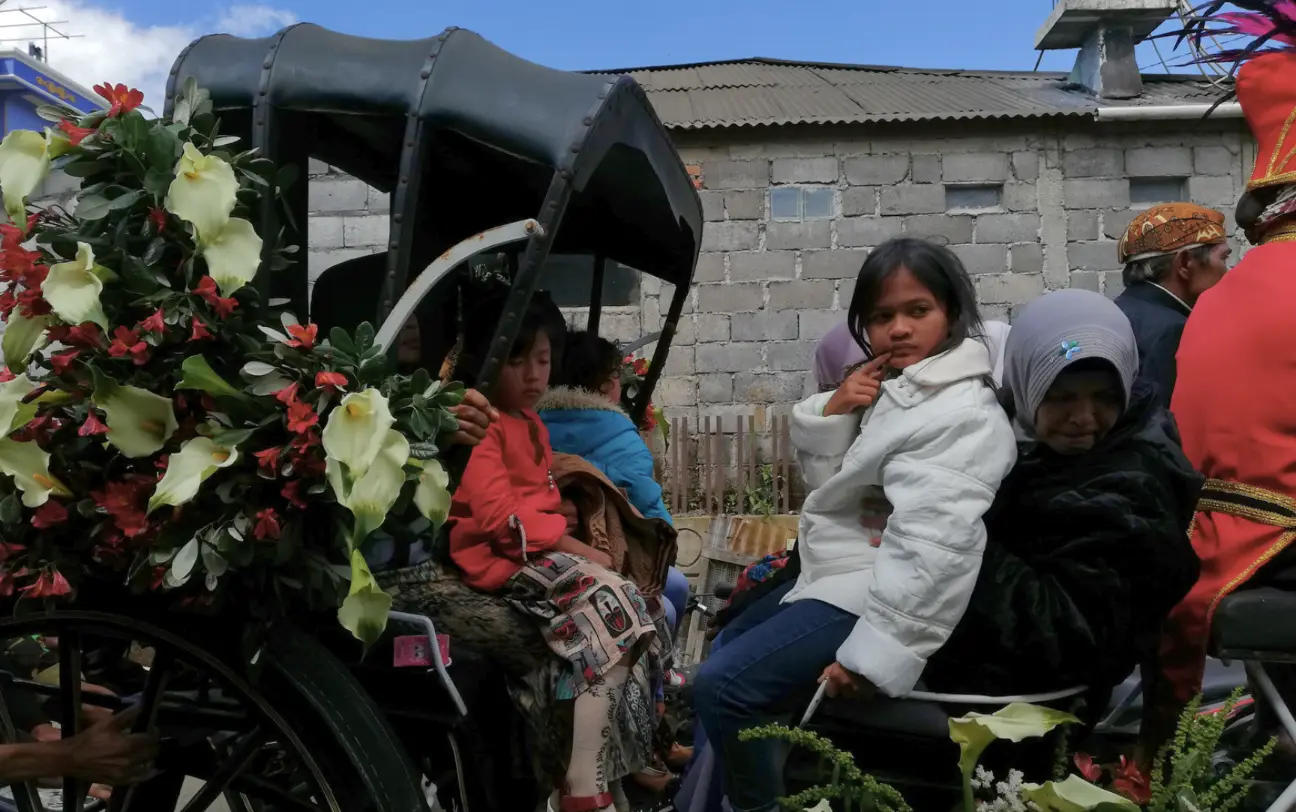 A dreadlocked child carried in a flower-decorated carriage during the Dieng Culture Festival ruwatan procession
